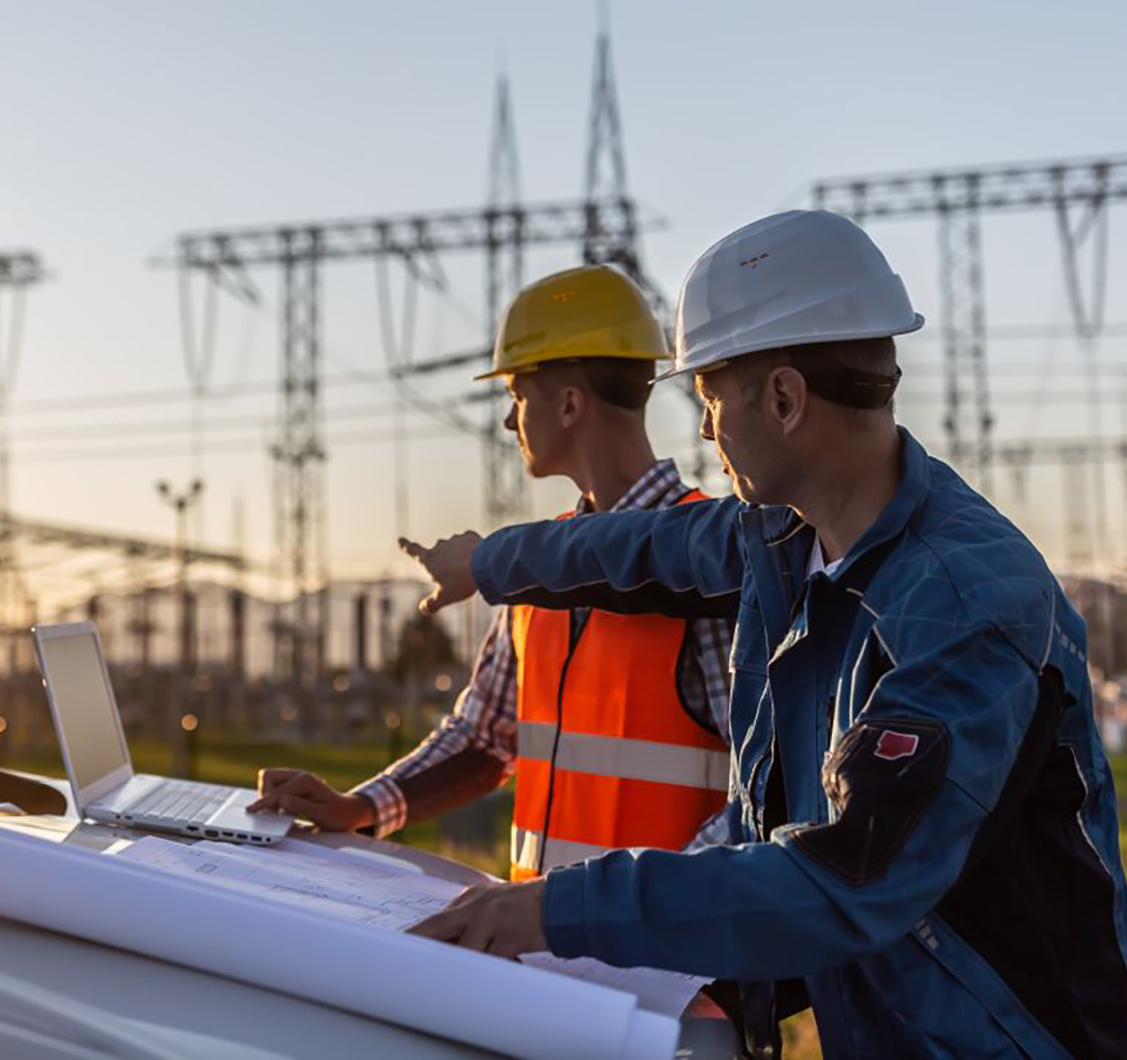 Two workers in hardhats surveying an electrical substation