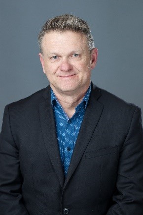 Mark Hanson is show from the chest up, wearing a ark blazer and blue shirt.